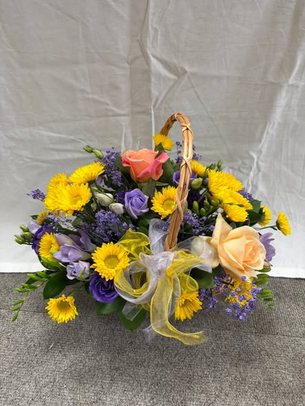 A basket arrangement of yellow chrysanthemums, lilac lisianthus and peach roses with a yellow ribbon, made by Bowbells Florist